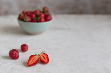Fresh ripe tasty strawberries. In the foreground are several berries. One berry is cut in half. In the background a lot of strawberries in a ceramic bowl with a dessert fork. Copy space.