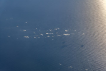 Fluffy clouds above the rippled ocean with sun reflection seen from an aircraft