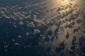 Fluffy clouds above the rippled ocean with sun reflection seen from an aircraft