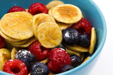 close up tiny pancakes with berries for breakfast in a blue bowl on white background. Home made trendy quarantine breakfast