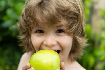 Portrait happy boy eats apple. Funny child holding an apple. Looking at camera. The concept of a healthy lifestyle, organic vegetarian food.