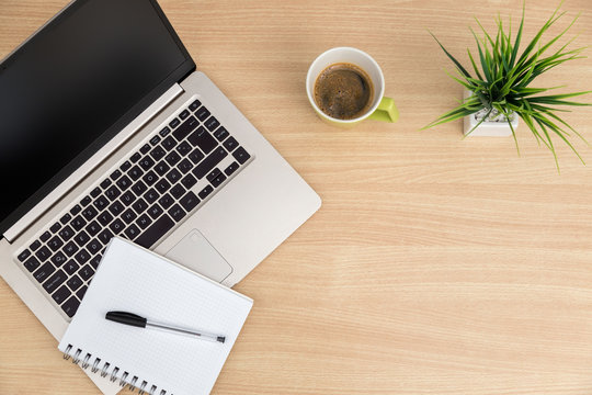 Top view of workspace. Table desk with laptop, coffee, notepad, pen and plant with empty space background for design. Flat lay view of light brown wooden desktop.