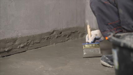 Waterproofing mortar on a concrete floor. A worker applies waterproofing to a concrete floor with a...