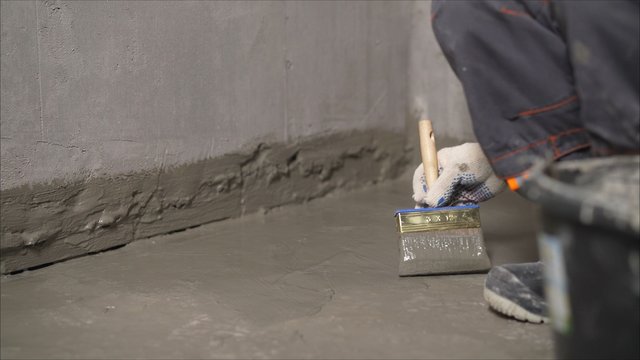 Waterproofing mortar on a concrete floor. A worker applies waterproofing to a concrete floor with a brush. Concrete floor repair.
