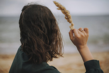 Mindfulness. Carefree hipster girl with windy hair holding herb on beach. Stylish tanned boho woman in modern outfit relaxing on seashore. Summer vacation.