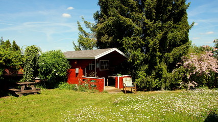 idyllisches rotes Gartenhaus in blühendem Garten unter blauem Himmel