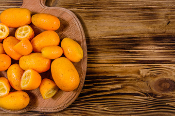 Cutting board with kumquat fruits on wooden table. Top view