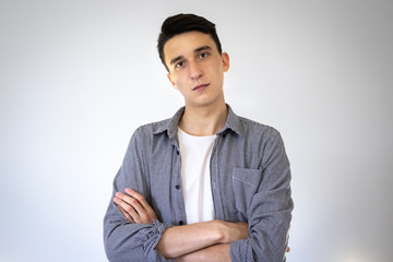 The thoughtful guy looks straight ahead with his arms crossed. On a gray background. In a shirt and a white t-shirt