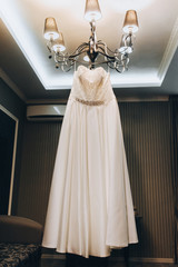 A beautiful white wedding dress of the bride hangs on a large chandelier in the interior. Photography, concept.