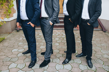 A company of stylish men in expensive suits stands with his hands in his pockets in nature. Wedding party of friends and groom. Advertising models. Photography, concept.