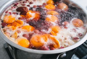 Fresh fruits: apricots, cherries, raspberries, apples are boiled in boiling water in a metal pan on a stove with bubbles and foam close-up. Cooking delicious homemade compote. Photography, concept.