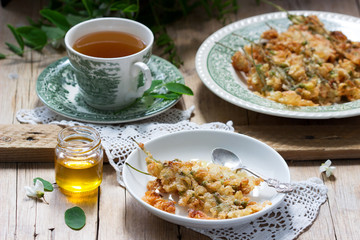 Robinia fritters served with tea and honey on a wooden table. Rustic style.