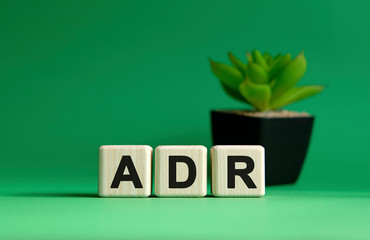 ADR - text concept on a green background. Wooden cubes and flower in a pot.