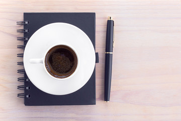 Notebook, pen and a cup of coffee on a wooden background. Coffee break. Top view with copy space, flat lay.