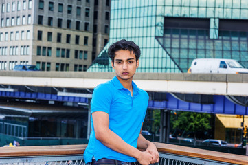 Portrait of 18 years old East Indian American teenager in New York City. Young male college student wearing blue short sleeve shirt, standing outside in business district,  relaxing, thinking..