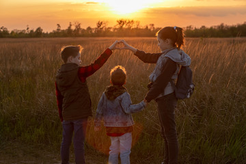 Children at sunset in the field show a heart from their fingers. Walk in the fresh air. Silhouette of three children. Beautiful sunset.