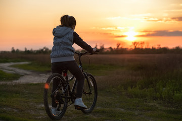 Fototapeta premium A teenage girl stopped to watch a beautiful sunset in a field. A walk on the bike . Active lifestyle.