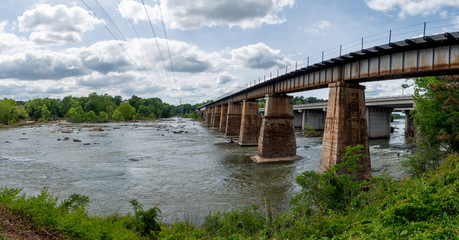 A railroad bridge made from stone and metal crossing the Broad River in Columbia, South Carolina taken from the Columbia Canal and Riverfront Park trail.