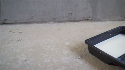 The primer is poured. Wall primer mix. A worker pours a primer from a black canister. The worker pours the primer into the tray.
