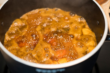 Apricot jam preparation in a black pot. Fruit preserve boiling in a big casserole with a wooden spoon. Close up.