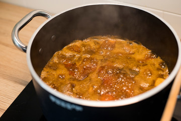Apricot jam preparation in a black pot. Fruit preserve boiling in a big casserole with a wooden spoon. Side view.