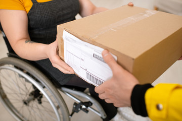 Close-up of unrecognizable deliveryman giving package to customer in wheelchair