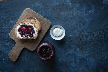 Sourdough bread toasts spread with cream cheese and raspberry jam on wooden board with blue background