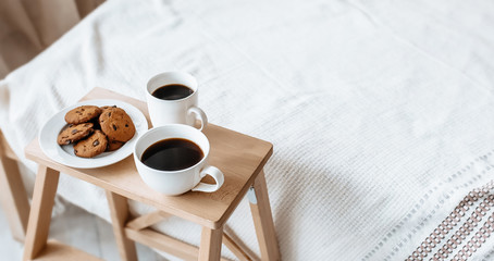 Breakfast in bed. Hot coffee with oatmeal cookies with chocolate on a wooden tray.