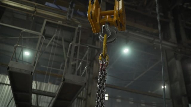 Low angle view of manual worker operating crane lifting sheet metal in industry. Crane in the factory lifts metal sheets