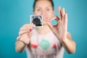 A young girl holds a condom in one hand, with the other hand shows an ok sign with her fingers