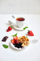 Mini-pancakes, Tiny pancakes, trendy food.
Fritters with fruit: blackcurrant, strawberry, mint. Breakfast with tea