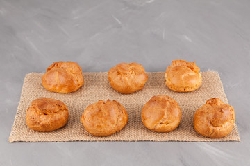 Fresh golden homemade buns (profiteroles) on a gray background with burlap