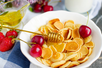 Tiny pancake cereal, cherry, strawberry, honey and milk on dark rustic background with lilac flowers