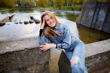 Beautiful portrait of a 90s redhead scandinavian teenager girl in jeans in a park near a lake
