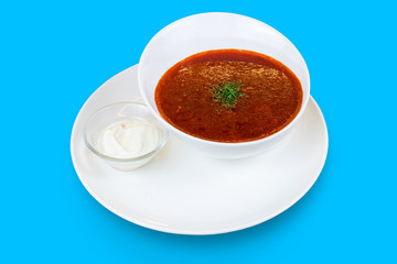 A bowl of borscht garnished with dill and sour cream isolated on blue background