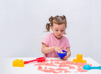 Portrait of a little girl playing with kinetic sand on a table on a white isolated background with space for text.