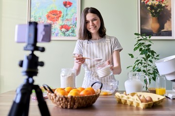 Girl teenager food blogger cooking orange pancakes at home in kitchen, smiling to the camera