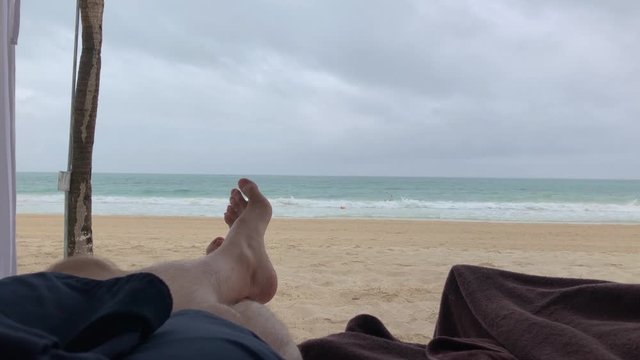 Ocean waves crashing on a beach as a person lays in a cabana enjoying the relaxing time.