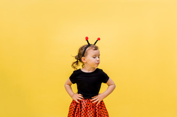 An aggrieved little girl in a ladybug costume on a yellow isolated background with space for text. Looking off to the side