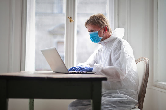 man works on computer protected by medical suit and mask