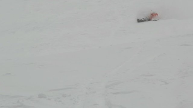 The skier is rapidly riding down a snowy slope and falling.