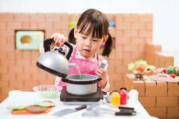 toddler girl pretend play food preparing role against cardboard blocks kitchen background