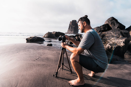 Male photographer with his camera and tripod adjusting the parameters to take a photograph at sunset on the beach of Benijo