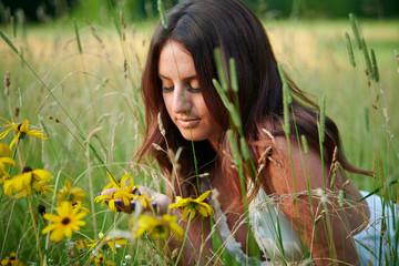 Stunning young Caucasian woman poses in white dressing field - summer fashion - pausing to admire...