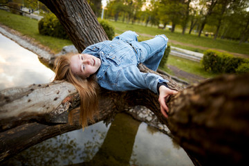 Redhead teen hippie girl authenticly lies on a tree above the water in the park
