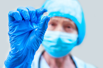 Doctor Scientist Woman in a medical equipment holding white round pills against coronavirus. Found treatment covid-19. Elderly pharmacist shows a of plain white tablets. Sensation. Pandemic ending