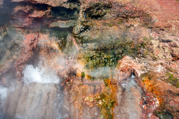 Boiling soil in geothermal area with hot steam and red volcanic textured rocks.