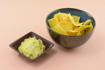 Salted crisp crunchy lentil chips and hummus dip snack food in bowls on pink background