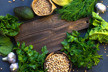 Vegetarian cooking concept of green fresh vegetables. A wooden board and next to a salad, parsley, avocado, chickpeas and lentils. Place for text