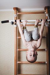 Home workout. The boy hangs head down on the horizontal bar.